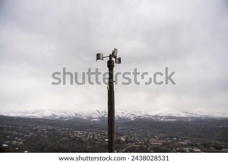 A solitary wind sensor perched atop a slender pole, stark against an overcast sky, silently monitors atmospheric conditions above an industrial complex. Its simplicity belies its importance in data co Royalty-Free Stock Photo #2438028531