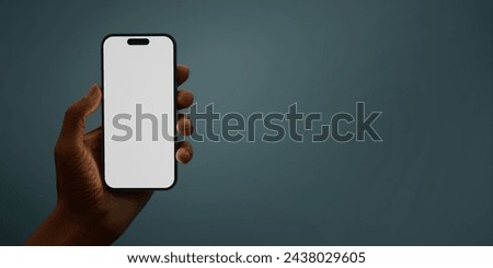 Black African-American hand displays a modern smartphone with a blank screen against a deep teal background, ideal for presenting apps or mobile interfaces in a clean and contemporary setting Royalty-Free Stock Photo #2438029605