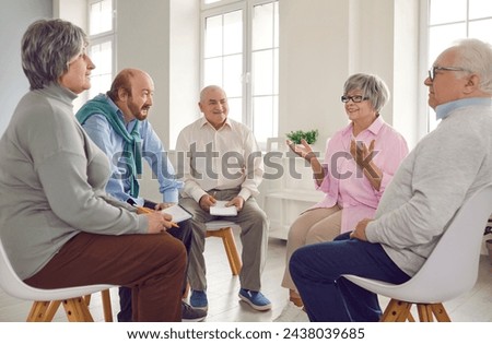 Several old people in group therapy at the retirement home. Senior men and women sitting in a circle, talking about their lives, sharing thoughts and ideas, and taking notes in paper notebooks Royalty-Free Stock Photo #2438039685