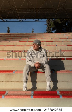Young sportsman sitting in the stands of a stadium alone listening to music early in the morning. Focusing concept and sport