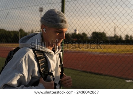 Young man arriving early in the morning at a sports facility to train. He walks in concentration listening to music. Copy space on the right in the background. Concept of focus and sacrifice.