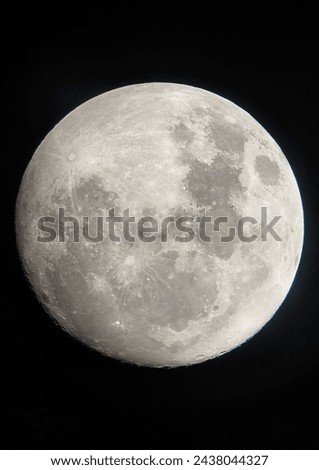A high-resolution picture of the bright full moon shines in the dark sky, revealing its bumpy surface adorned with dark spots and bright spots reflecting light.