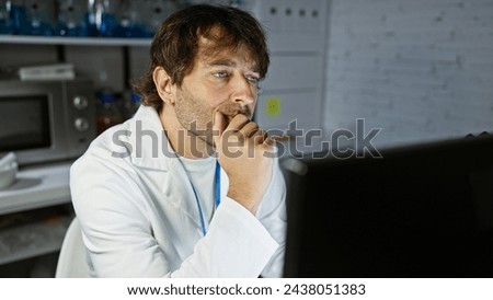 Pensive man with beard in lab coat analyzing data on computer in laboratory setting Royalty-Free Stock Photo #2438051383