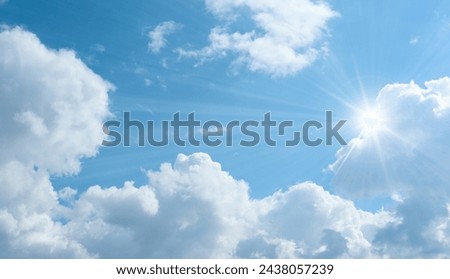 Bottom up view of blue sky with shining sun. White fluffy clouds on a blue sky in spring season.