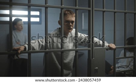 Portrait of diverse teenage prisoners behind metal bars in prison cell looking at camera. Multiethnic young inmates serve imprisonment terms in jail. Juvenile detention center or correctional facility Royalty-Free Stock Photo #2438057459