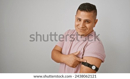 Cheerful young latin man pointing at his diabetes sensor, smiling proudly on white isolated background, embracing comfortable glucose monitoring technology Royalty-Free Stock Photo #2438062121