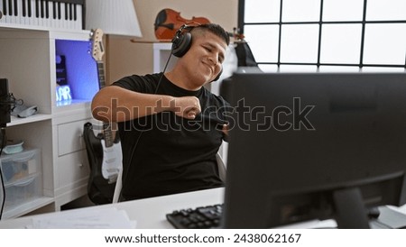 Passionate young latin man, an alluring musician, lost in the melody of his song in the cozy corner of a music studio, dancing while listening with headphones with an infectious smile. Royalty-Free Stock Photo #2438062167