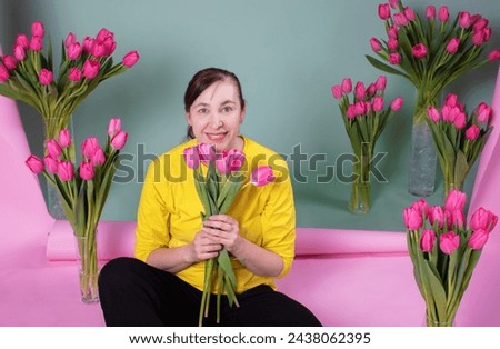 A happy middle-aged woman with a bouquet of tulips is happy and smiling on a pink-green background. Royalty-Free Stock Photo #2438062395