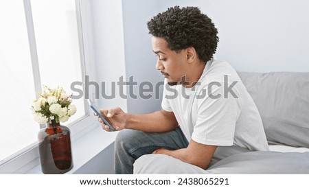 A young adult man with curly hair using a smartphone in a modern living room with a bouquet background