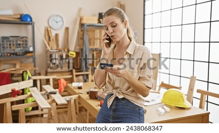 A young woman multitasking on the phone while holding a credit card in a carpentry workshop.
