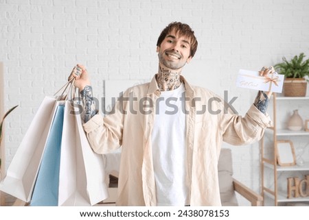 Young tattooed man with gift card an shopping bags at home