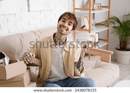 Young tattooed man with gift card and new shoes sitting on sofa at home