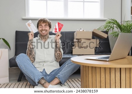 Happy young tattooed man with gift cards sitting at home