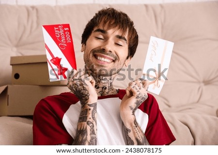 Young tattooed man with gift cards at home, closeup