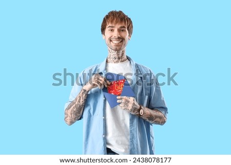 Young tattooed man with gift card in envelope on blue background