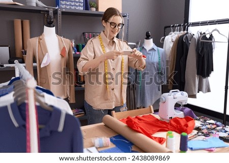 Young caucasian woman tailor make photo by smartphone to t shirt at atelier