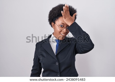 Beautiful african woman with curly hair wearing business jacket and glasses surprised with hand on head for mistake, remember error. forgot, bad memory concept.  Royalty-Free Stock Photo #2438091483