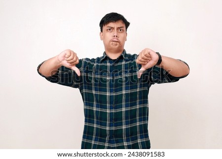 Photo of unsatisfied young asian man show two thumbs down bad mood sullen isolated on white background Royalty-Free Stock Photo #2438091583