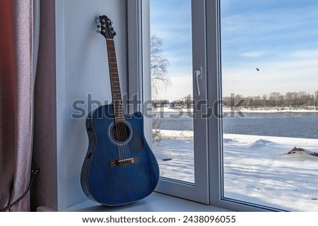 Dreadnought acoustic guitar is on window sill by the window.