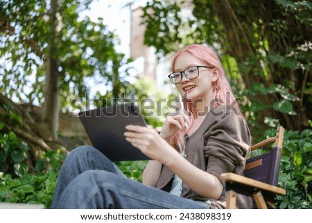 Cute pink hair girl drawing on digital tablet in garden, Woman Doing Freelance Work in Garden, woman with digital tablet with artwork.