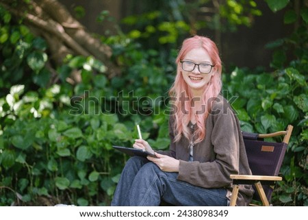 Cute pink hair girl drawing on digital tablet in garden, Woman Doing Freelance Work in Garden, woman with digital tablet with artwork.