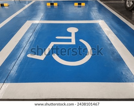 Special parking spaces in department stores have a blue background and a white disabled person symbol in a square frame for wheelchair users. The car park has yellow Brake barrier devices at the back.