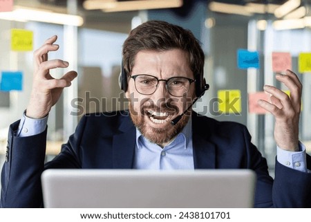 An overwhelmed businessman in a headset shows frustration while working at his desk filled with sticky notes in a modern office.