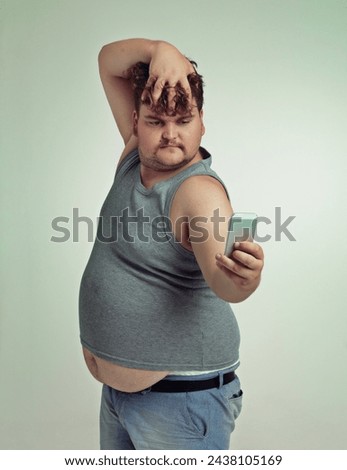 Selfie, cellphone and plus size man in studio posing with casual, trendy and cool outfit with stomach. Phone, serious and funny with male person with photography picture isolated by gray background.