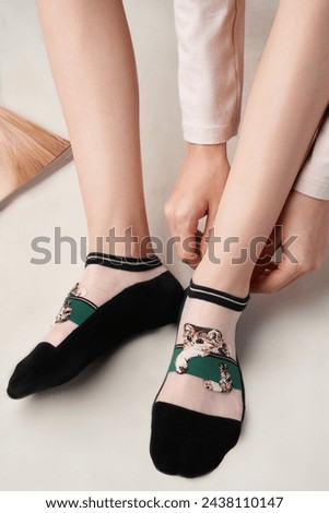 Close-up of a woman's legs wearing white and black printed socks. The girl is posing on a pastel background. Nylon socks with cat-print on the feet of a beautiful woman. Front view.