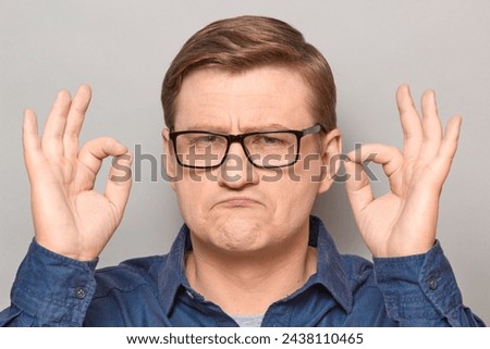 Studio close-up portrait of proud confident blond mature man with glasses, showing okay gestures with both hands, expressing his approval and acceptance. Headshot over gray background