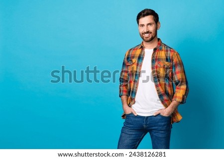 Photo of good mood stylish man dressed plaid shirt hold hands in pockets near promotion empty space isolated on blue color background