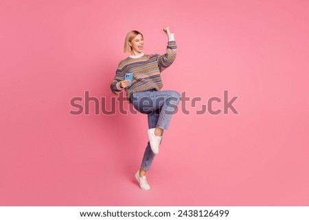 Full size photo of ecstatic girl wear ornament sweater jeans hold smartphone raising fist up win lottery isolated on pink color background