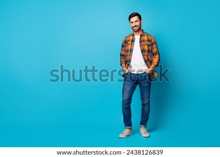 Full size photo of satisfied man dressed plaid shirt hold palms in pockets stand near offer empty space isolated on blue color background
