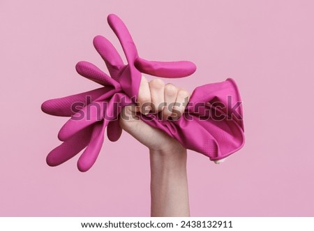 Woman's hand holding rubber cleaning gloves on pink background