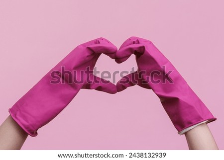 Hands in purple rubber cleaning gloves heart shape on a pink background. House cleaning and housekeeping concept