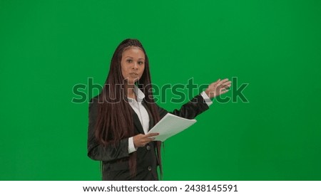 Female reporter isolated on chroma key green screen background. African American woman news host in suit with paper documents talks at camera.