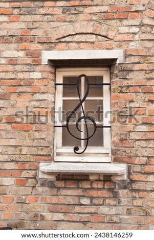 Window with a lattice in the form of a treble clef against the background of an old brick wall. Bruges. Flanders. Belgium. Royalty-Free Stock Photo #2438146259