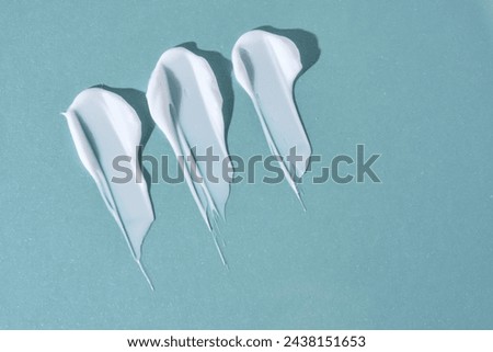 Three strokes of white cream on a blue background. Royalty-Free Stock Photo #2438151653