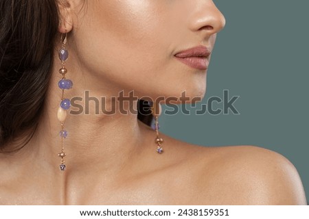 Gold earring with blue and purple chalcedony stones on jewelry model closeup.  Royalty-Free Stock Photo #2438159351
