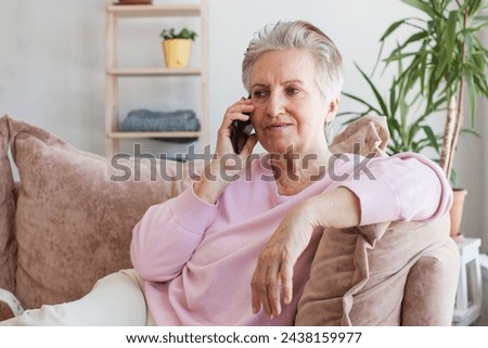 Relaxed mature old 70s woman, older middle aged female customer holding smartphone using mobile app, talking on cell phone technology device sitting on couch at home.
