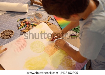 Overhead view of a teenage school boy drawing on paper with pastel color pencils, creating a background for further during art class
