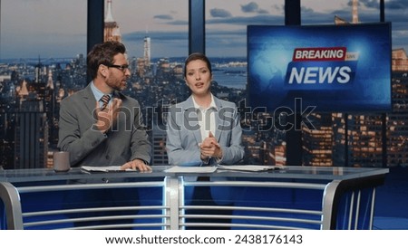 Emotional news readers discussing live tv newscast in night media studio closeup. Positive charismatic presenters smiling communicating with audience. Cheerful couple anchors talking daily reportage
