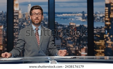 News presenter broadcasting studio. Positive bearded anchor man gesturing hand bringing up important day events. Authority announcer sharing latest evening updates delivering information at work  Royalty-Free Stock Photo #2438176179