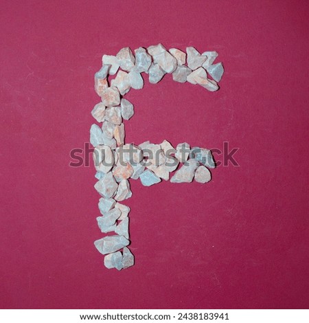 Letter F made of white stones. Creative alphabet concept on a red background. 