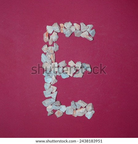 Letter E made of white stones. Creative alphabet concept on a red background. 