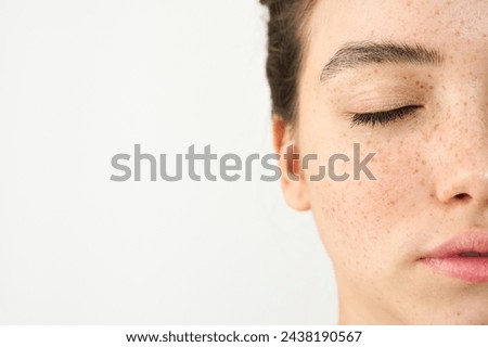 Close up aesthetic beauty half face portrait of Latin girl isolated on white background. Young adult pretty brunette Hispanic woman model with freckles eyes closed. Skincare cosmetic, skin care.