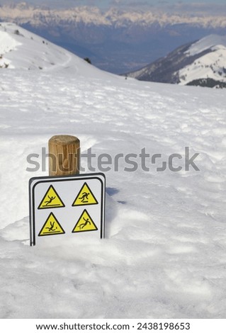 caution sign danger of slipping and falling near ravine with white fresh snow in mountains
