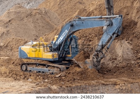 A crawler excavator is at work, the bucket is filled with soil. The machine ensures the development of land at the construction site. The excavator shows signs of dirt and wear, indicating heavy use Royalty-Free Stock Photo #2438210637