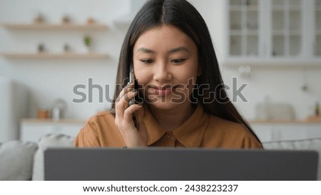 Asian Chinese multitasking businesswoman korean woman working laptop from home solve business task talk mobile phone listen information nod head agree make order delivery in kitchen talking cellphone Royalty-Free Stock Photo #2438223237