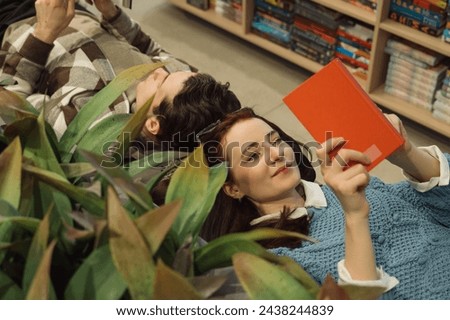 Young couple relaxing among plants in a bookstore browsing books together. Royalty-Free Stock Photo #2438244839